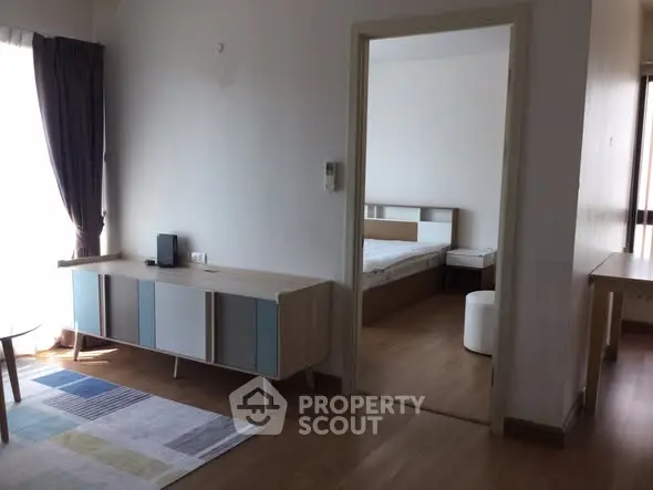 Modern apartment interior with open living room and bedroom view, featuring stylish furniture and natural light.