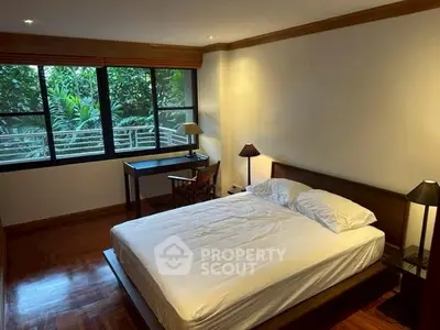 Spacious bedroom with large window and garden view, featuring elegant wooden flooring and modern furnishings.
