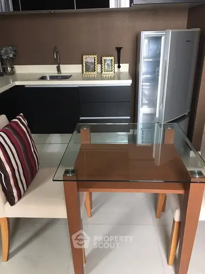 Modern kitchen with sleek black cabinets, glass dining table, and open fridge showcasing contemporary design.