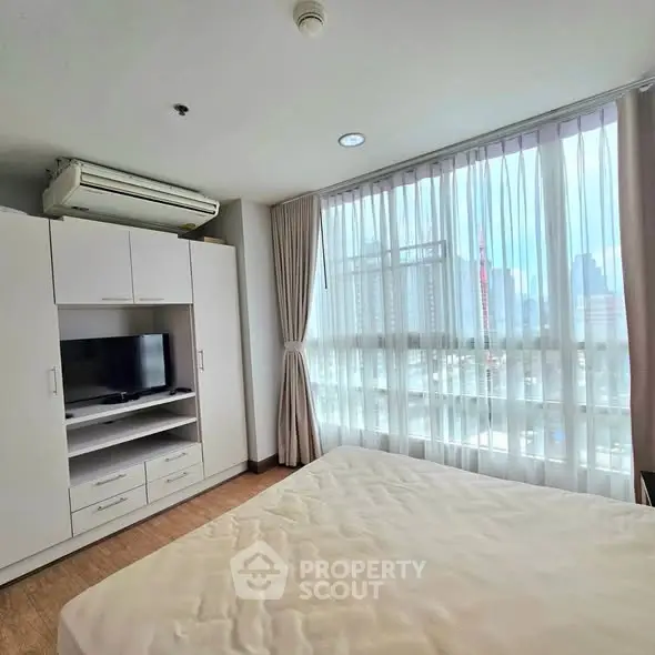 Bright bedroom with large windows and city view, featuring a built-in wardrobe and air conditioning.