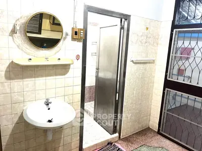 Spacious bathroom with modern fixtures and tiled walls, featuring a round mirror and stainless steel door.