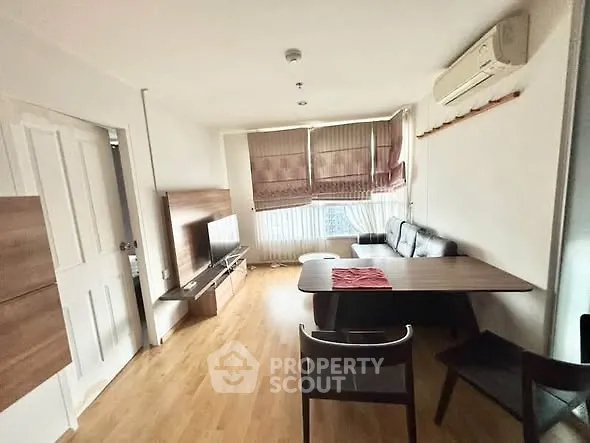 Cozy living room with wooden flooring, modern furniture, and natural light from large windows.