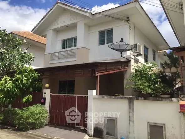 Charming two-story house with lush greenery and gated entrance in a serene neighborhood.