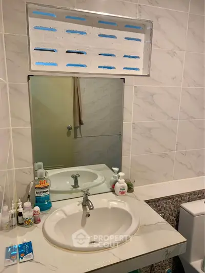 Modern bathroom with stylish sink and mirror, featuring elegant tile design and essential toiletries.