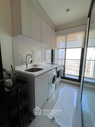 Modern kitchen with sleek cabinetry and washing machine, featuring large window for natural light.