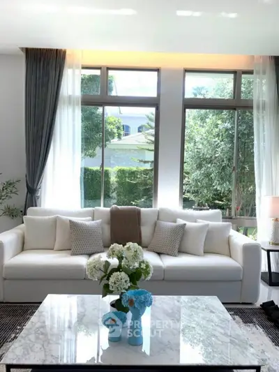 Elegant living room with large windows, white sofa, and marble coffee table, offering a bright and inviting atmosphere.