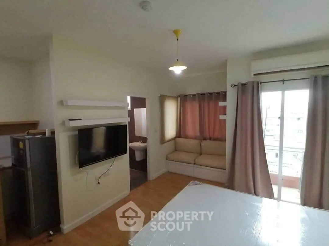 Cozy living room with TV, fridge, and balcony access in modern apartment.