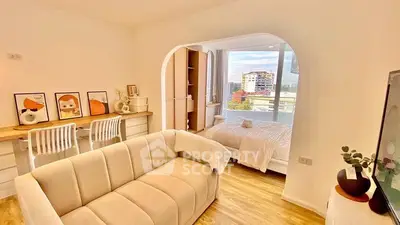 Modern open-plan living room with cozy seating and a view of the bedroom, featuring stylish decor and natural light.