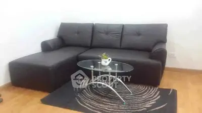 Modern living room with sleek black sofa and stylish glass coffee table on wooden flooring.