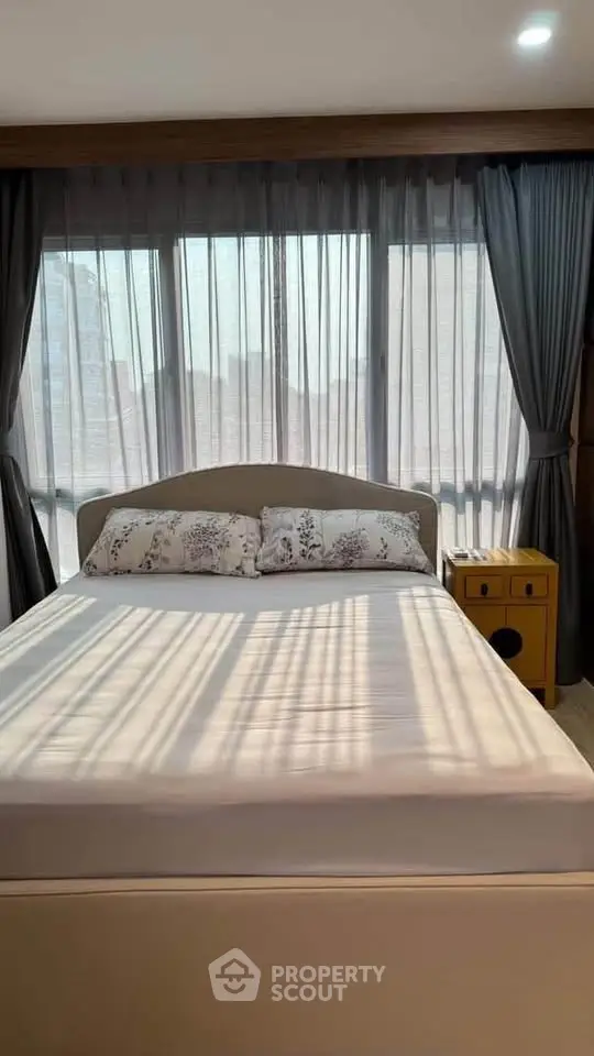 Cozy bedroom with large windows and elegant curtains, featuring a comfortable bed and stylish decor.