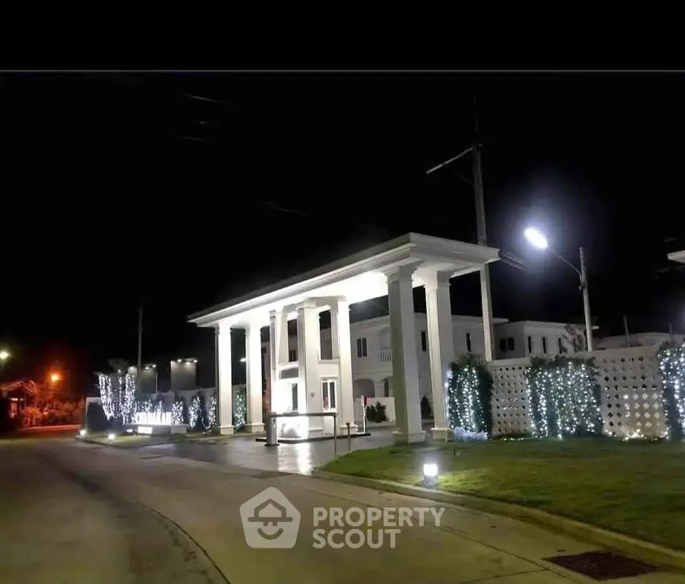 Elegant night view of a grand entrance with illuminated columns and lush landscaping.