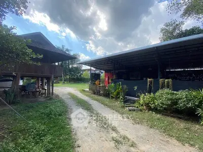 Charming rural property with lush greenery and rustic structures under a cloudy sky.