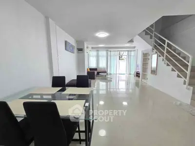 Spacious modern living room with dining area and staircase, featuring sleek design and ample natural light.