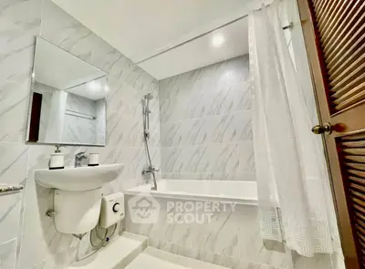 Modern bathroom with sleek white tiles and bathtub in a stylish real estate property.