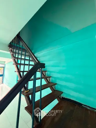 Spacious interior staircase with vibrant turquoise walls and wooden steps, ideal for modern urban living.