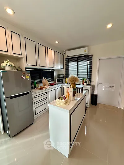 Modern kitchen with sleek cabinetry and island, featuring stainless steel fridge and stylish decor.
