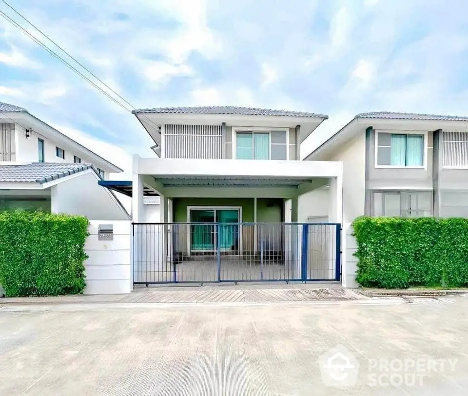 Modern two-story house with gated entrance and lush greenery