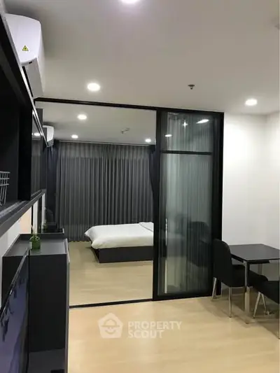 Modern studio apartment with glass partition and cozy bedroom setup.
