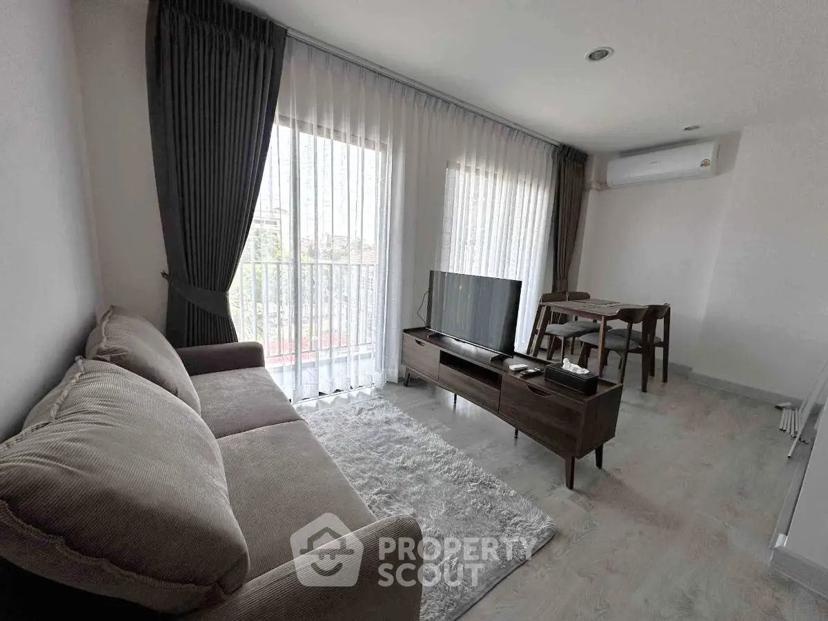 Modern living room with cozy sofa, TV, and dining area, featuring large windows and natural light.