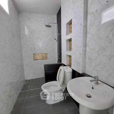 Modern bathroom with sleek design, featuring a shower, toilet, and sink with elegant marble walls.