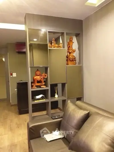 Modern living room with stylish shelving and decorative statues, featuring a comfortable leather sofa and wooden flooring.