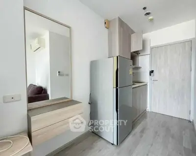 Modern compact kitchen with sleek cabinetry and stainless steel fridge in a bright apartment.