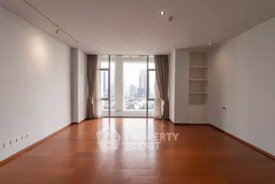 Spacious empty living room with wooden floors and large windows offering city views.
