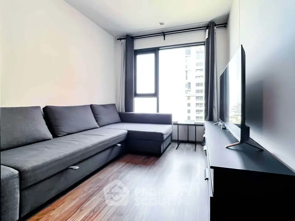 Modern living room with sleek furniture and large window offering city views.