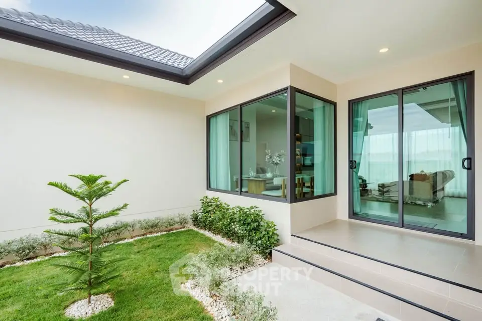 Modern home exterior with lush garden and large glass doors leading to a stylish living room.