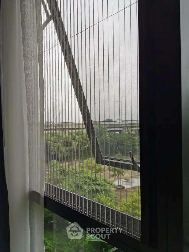Modern window with insect screen overlooking lush greenery and urban landscape.