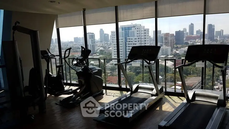 Modern gym with city view in high-rise building, featuring treadmills and exercise equipment.