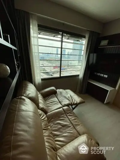 Cozy living room with plush leather sofa and built-in bookshelves, boasting a large window with an urban view, perfect for relaxation and reading.