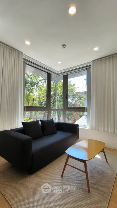 Modern living room with corner windows and black sofa, offering a bright and inviting atmosphere.