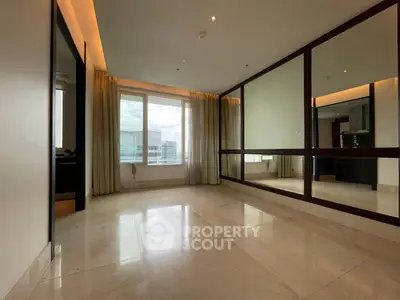 Spacious modern living room with large windows and mirrored wall, offering city views and abundant natural light.