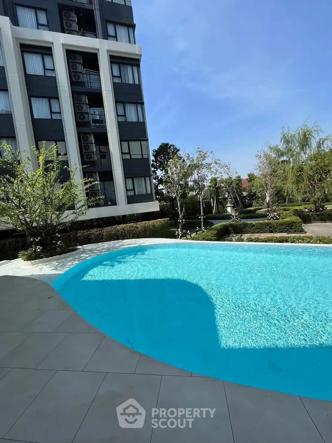 Luxurious apartment building with sparkling pool and lush garden view.