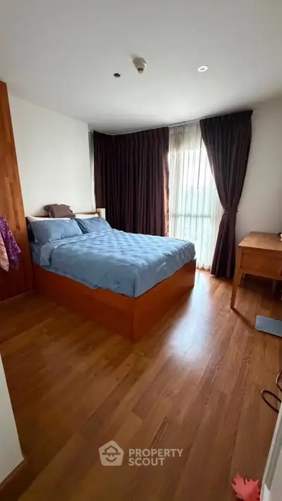 Cozy bedroom with wooden flooring and large window with curtains, perfect for relaxation.