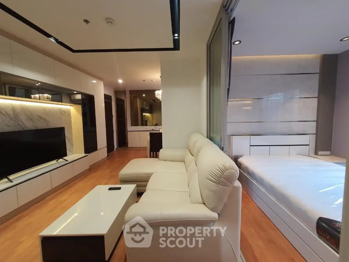 Modern open layout living room with adjacent bedroom, featuring sleek furniture and stylish decor.