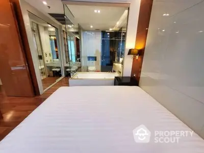 Luxurious bedroom with sleek hardwood floors leading to an en-suite bathroom featuring a glass-enclosed shower and modern amenities.