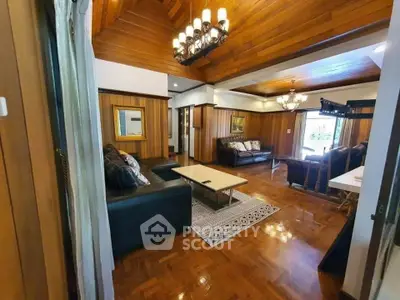 Luxurious living room with wooden paneling and elegant chandeliers, featuring spacious seating area and polished floors.