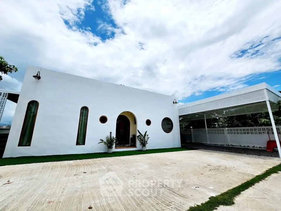 Modern minimalist white house with unique window design and spacious driveway under a bright blue sky.