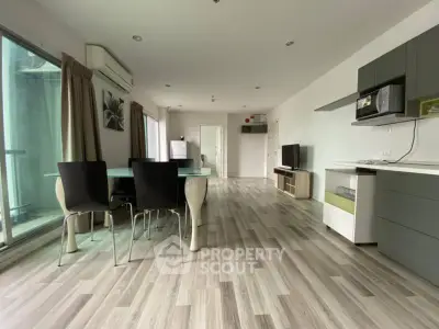 Spacious modern living room with open kitchen and dining area, featuring sleek furniture and large windows.