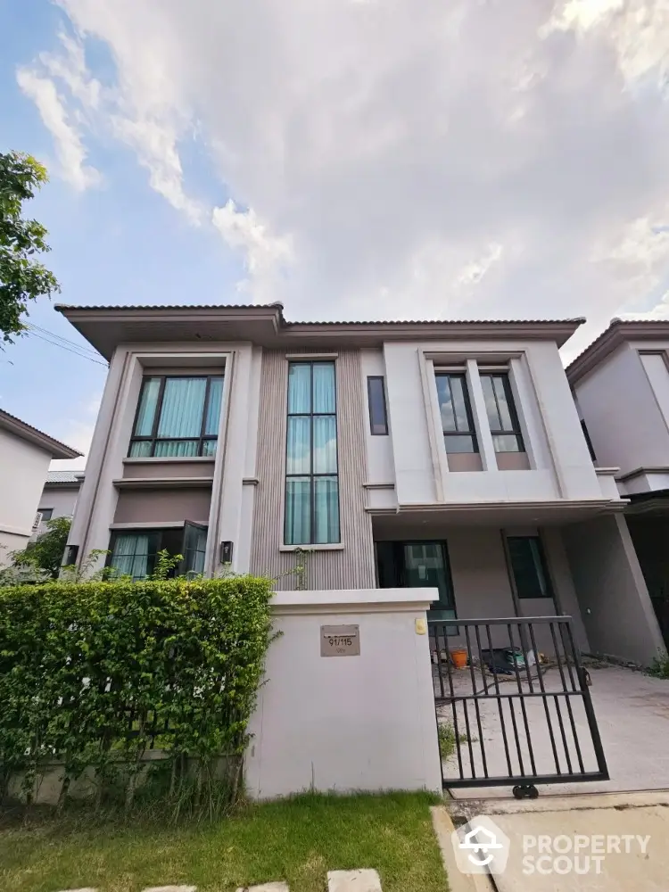 Modern two-story house with large windows and gated entrance in suburban neighborhood.