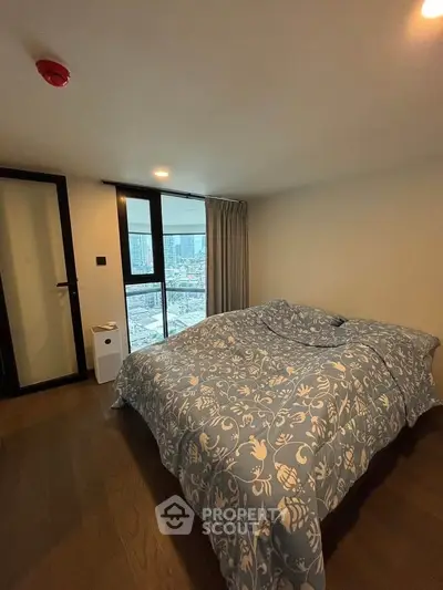 Cozy bedroom with city view, featuring a large window and stylish bedding in a modern apartment.
