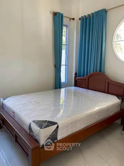 Bright bedroom with wooden bed frame and blue curtains, featuring a large window for natural light.