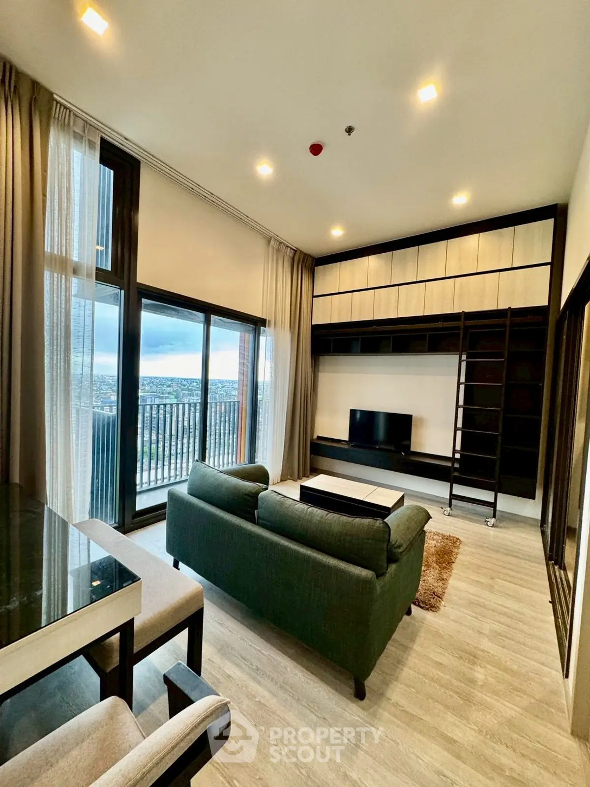 Modern living room with large windows and city view, featuring stylish furniture and built-in shelving.