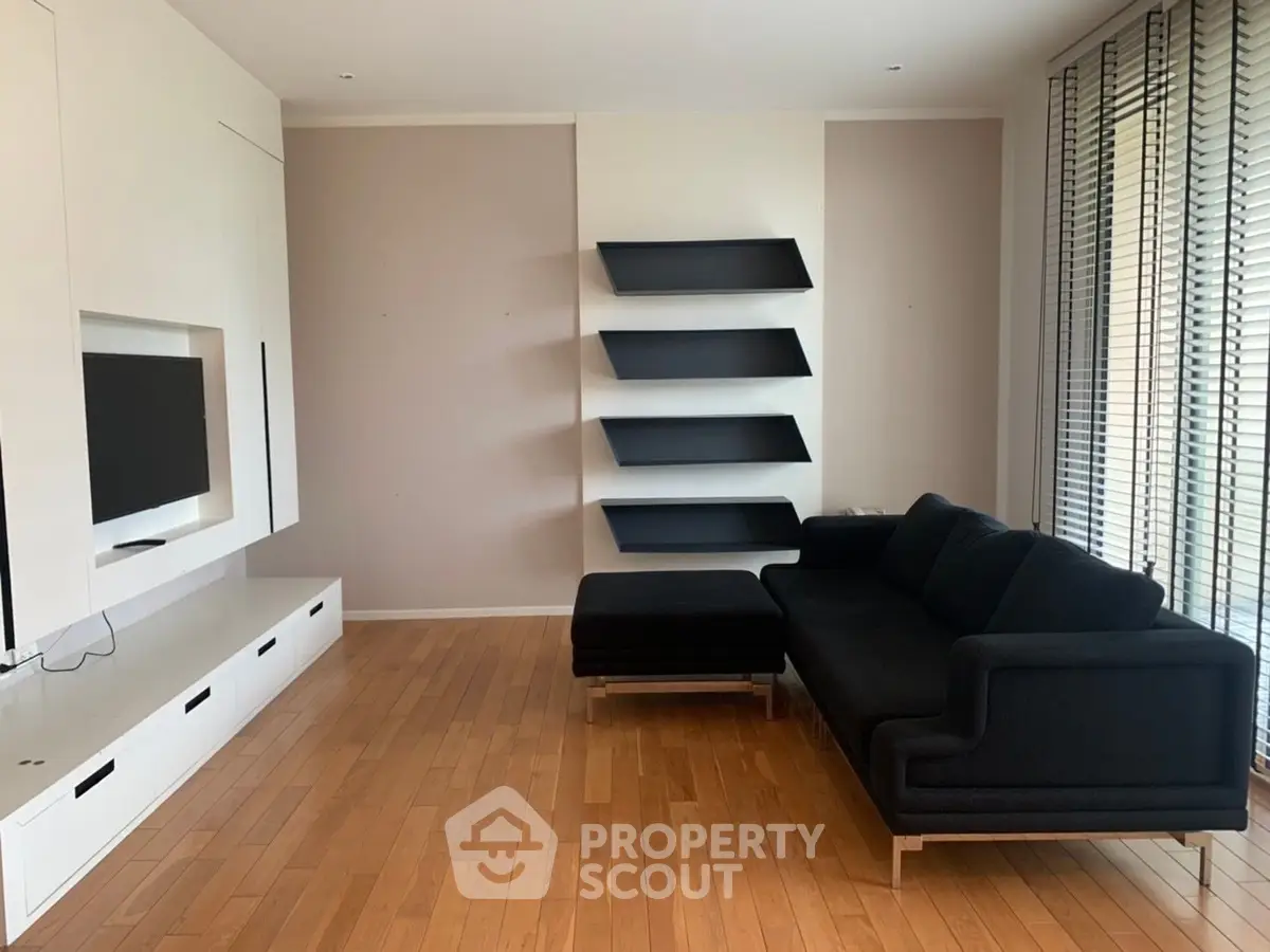 Modern living room with sleek black sofa and wall-mounted TV, featuring minimalist design and wooden flooring.