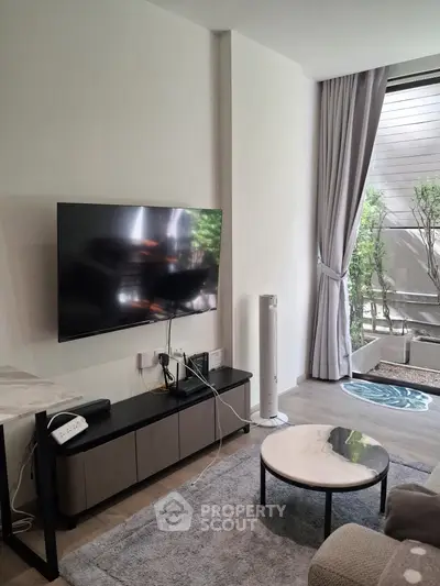 Modern living room with sleek TV setup and cozy decor, featuring a view of a private garden area.