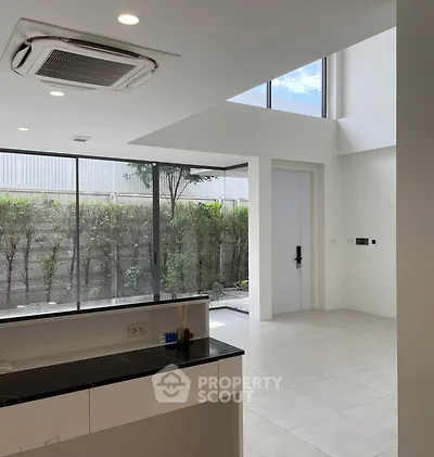 Modern open-layout kitchen with large windows and garden view, featuring sleek design and abundant natural light.
