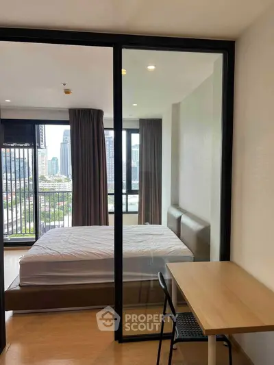 Modern bedroom with city view and glass partition, featuring a cozy bed and study desk.