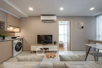 Modern living room with integrated kitchen and washing machine, featuring sleek design and neutral tones.